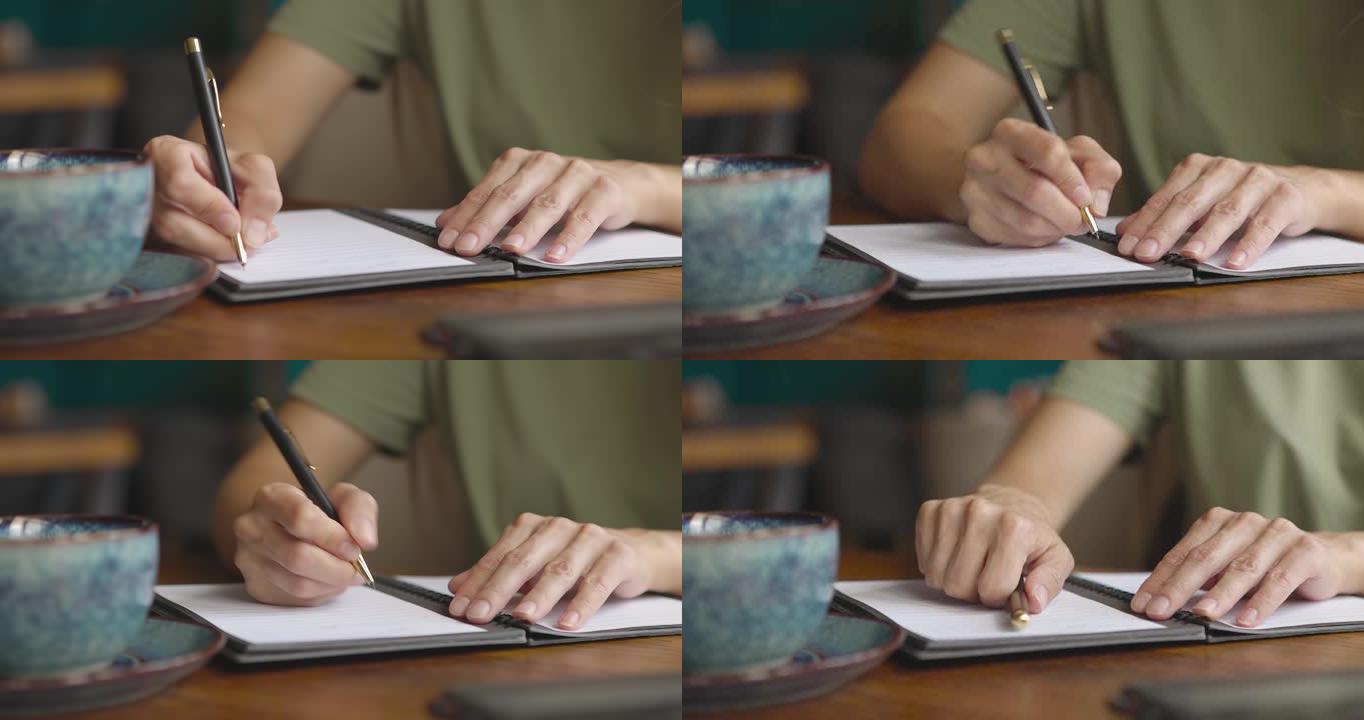 女人的手在桌上放着咖啡杯和笔记本电脑的纸质笔记本上写下