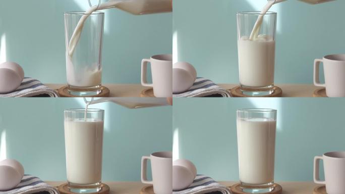 厨房桌子上有鸡蛋，杯子和将牛奶倒入蓝色墙前的玻璃中。牛奶视频合成。