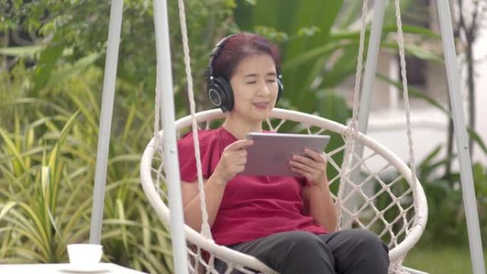 中年妇女在秋千上放松，在ba的平板电脑上听音乐