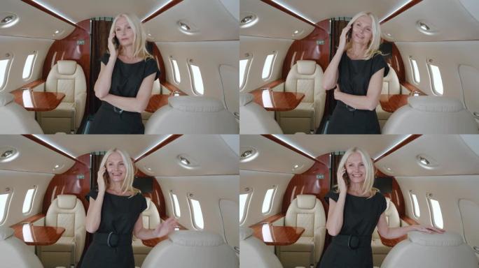 快乐成功的成熟女商人站在私人飞机上用手机聊天。微笑的有钱的高级女性在享受头等舱航空公司的豪华旅行时使
