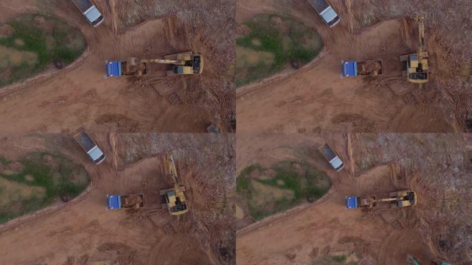 鸟瞰式挖掘机在施工现场挖掘土壤并将其装载到卡车上。