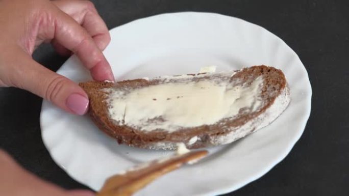 女人用木制的手在一块面包上撒上柔软的黄油。