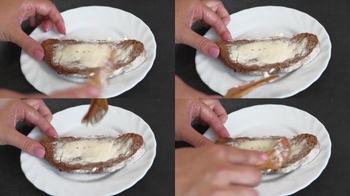 女人用木制的手在一块面包上撒上柔软的黄油。