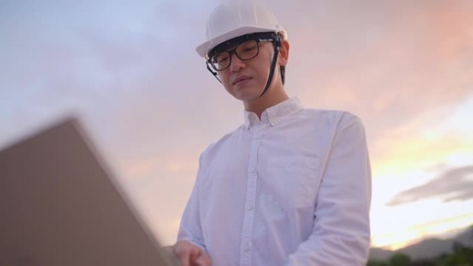 亚洲工程师戴安全防护安全帽在空旷的建筑工地与笔记本电脑一起工作，工程许可证，结构规划分析，日落而息的