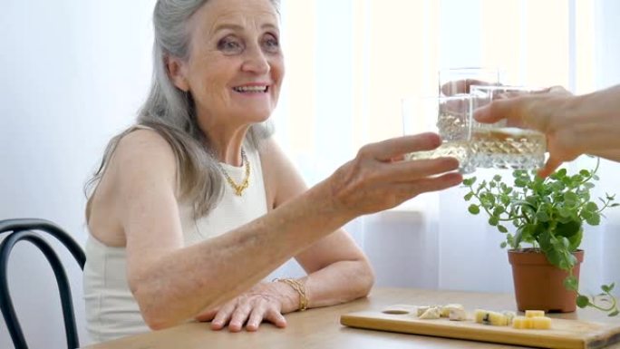 老年母亲在家里说话喝酒碰杯的女性肖像坐在桌旁，退休快乐，母亲节概念，酒瘾