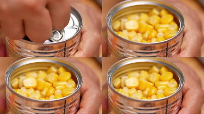 双手用玉米粒打开锡罐，特写。显示如何用拉环打开一个罐。玉米罐头食品不易腐烂的食物储存产品在家庭厨房。