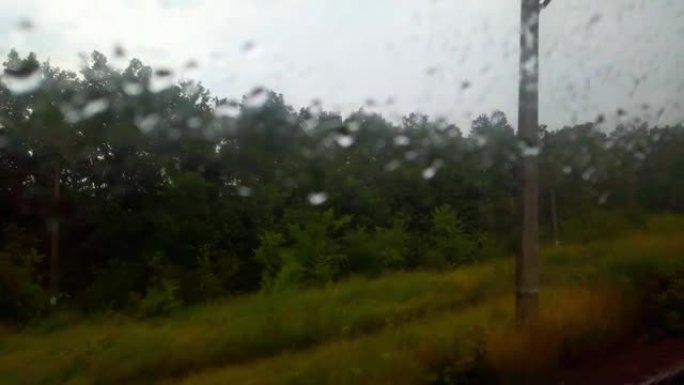 通过铁路车厢的湿玻璃拍摄乡村景观。窗外下雨，玻璃上有水滴。