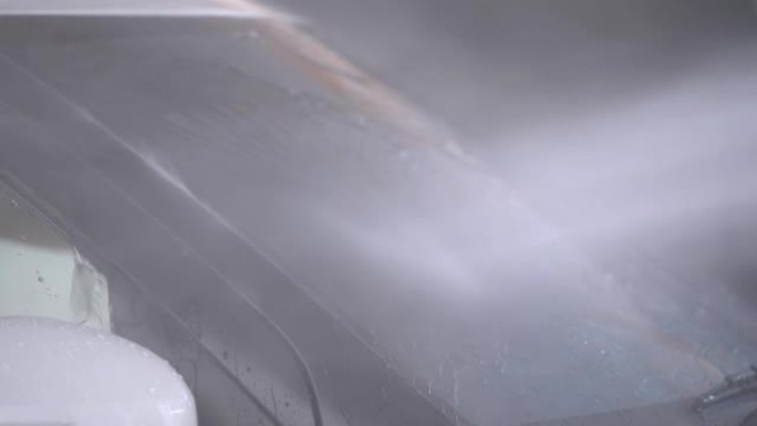 水雾清洗一辆白色汽车。关闭车库部分车辆侧门和前玻璃的喷水清洗。在车辆上使用喷水喷雾的工人。
