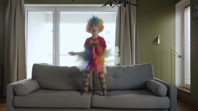 小丑在客厅玩耍。穿着小丑服装的有趣快乐的小女孩在家里的沙发上跳舞和跳跃。热爱生活方式之家。快乐有趣的