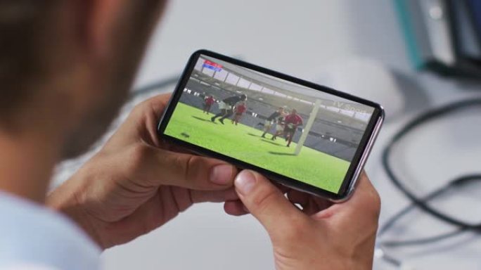 男性医生在智能手机上观看橄榄球比赛的合成