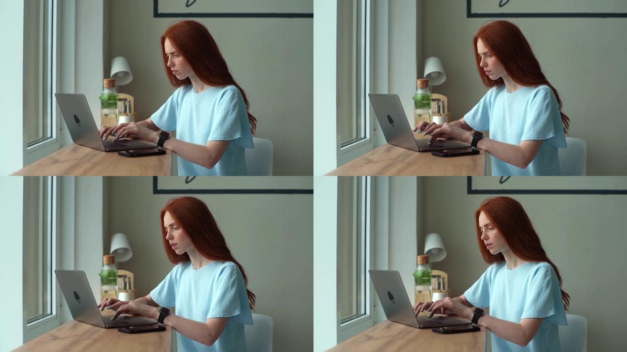 严肃的红发年轻女性自由职业者在咖啡馆坐在桌边的笔记本电脑上思考。