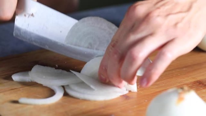 厨师用小刀在木板上切白洋葱。