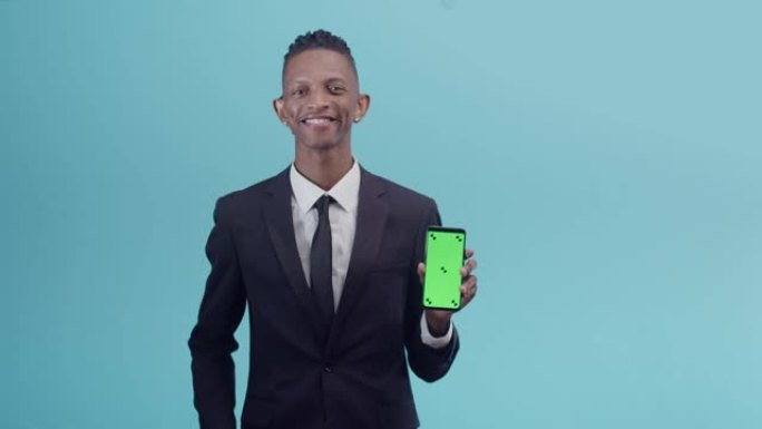 穿着办公室西装的黑人拿着带有应用程序的手机，微笑着用手指显示屏幕，工作室的蓝色背景。Chromake