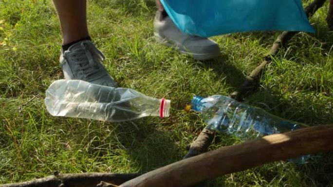 特写男性志愿者的手在公园或森林的袋子里收集塑料瓶。环保志愿者正在清扫乡村。