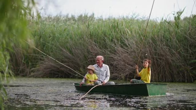 与孩子们一起在大自然中休息，祖父和孙子在绿色芦苇和水的风景背景下在河上钓鱼