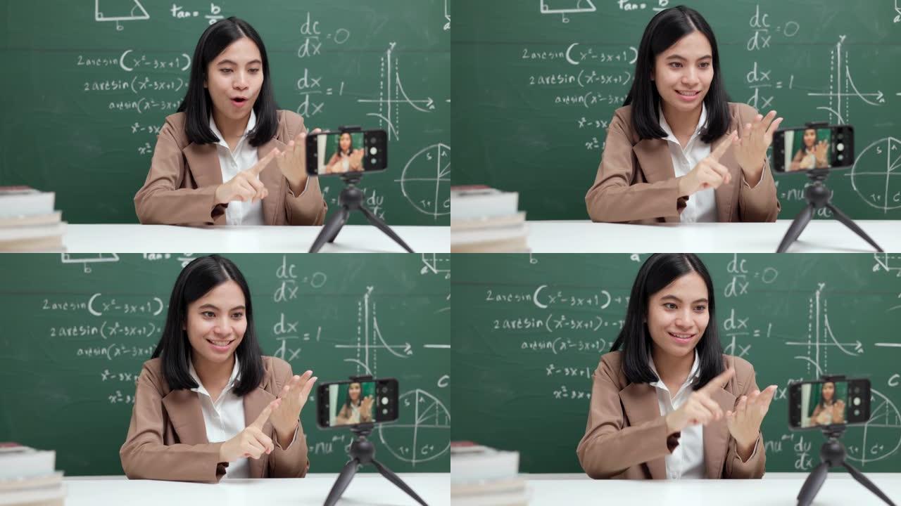 年轻的亚洲教师妇女坐和与学生的视频会议。女教师通过智能手机在线课程从直播中培训课堂数学。