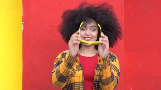 4k视频美丽的非洲裔美国女人，非洲头发，黄色太阳镜和彩色衣服在蓝色背景上微笑