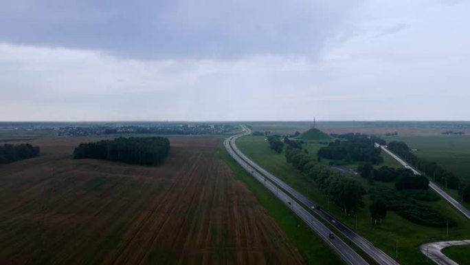 道路和运输的鸟瞰图。人们在高速公路上开车旅行。背景上的白俄罗斯荣耀纪念碑。戏剧性的天空。物流和旅行概