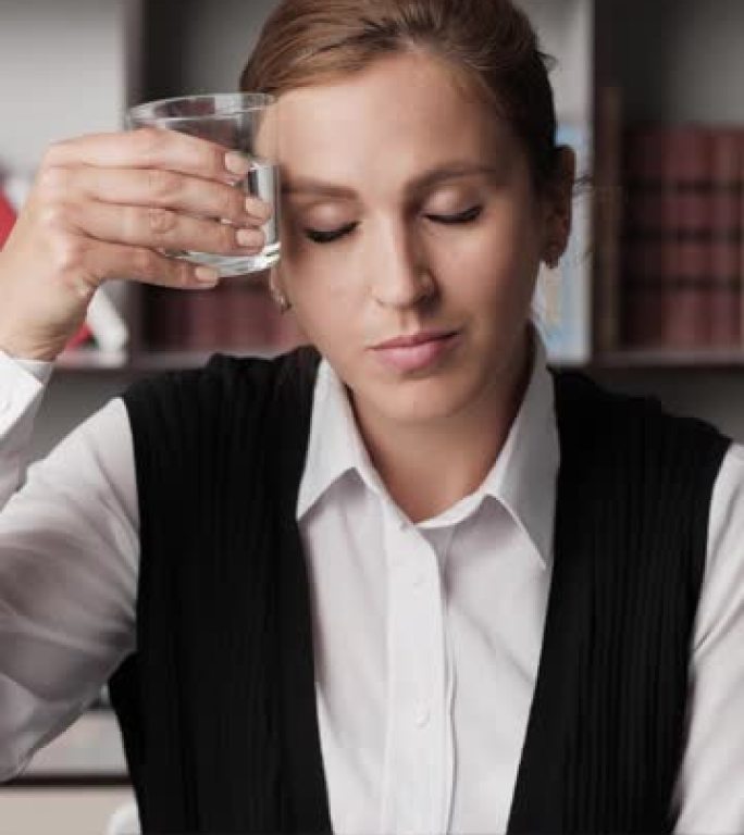 宿醉，酒精成瘾，酒精概念。垂直视图沮丧的有吸引力的女性办公室工作人员在工作场所患有宿醉，喝水和类型的