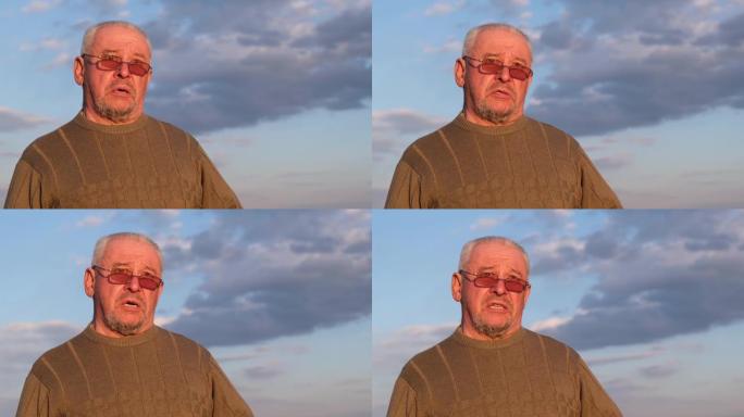 一个穿着灰色毛衣和太阳镜的老人在蓝天下。