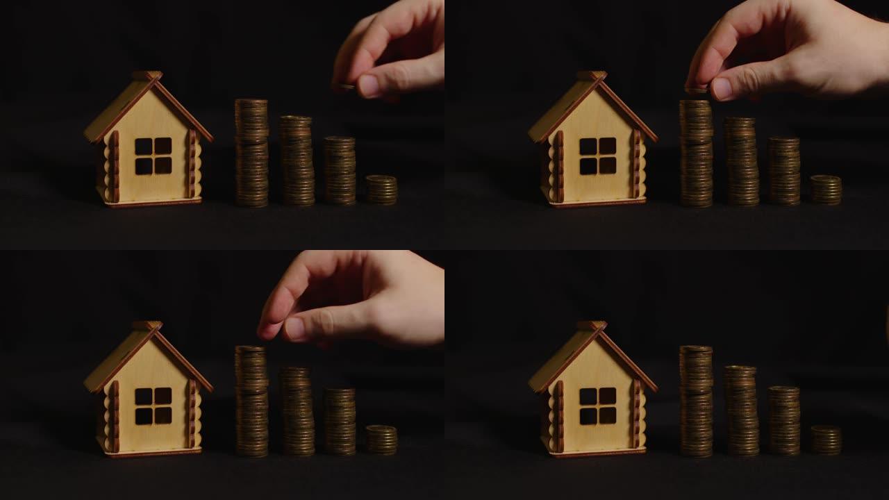 黑色背景上有硬币列的小木屋。人手把硬币放在柱子上。购买新公寓和屋顶的概念