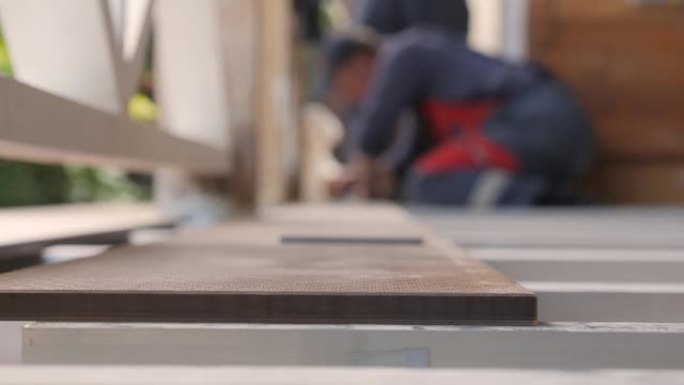 地板安装露台。木匠在木板上画了一条切割线。用角尺关闭测量地板。木匠用铅笔和仪表标记在木板上测量。维修