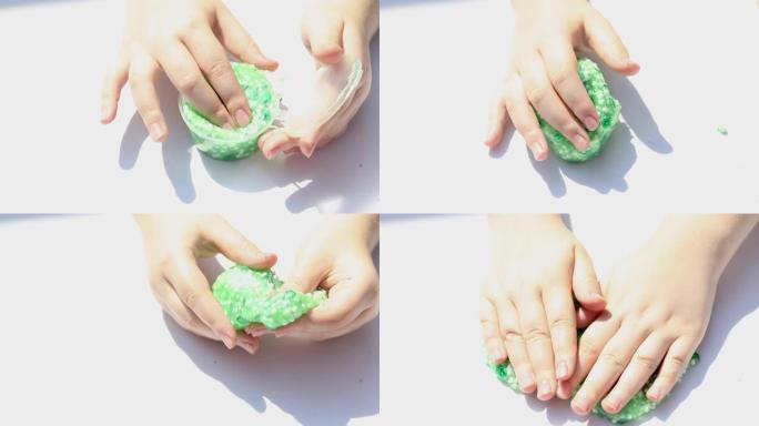 一个小女孩的手玩着闪亮的绿色粘液，将其从容器中拉出，特写