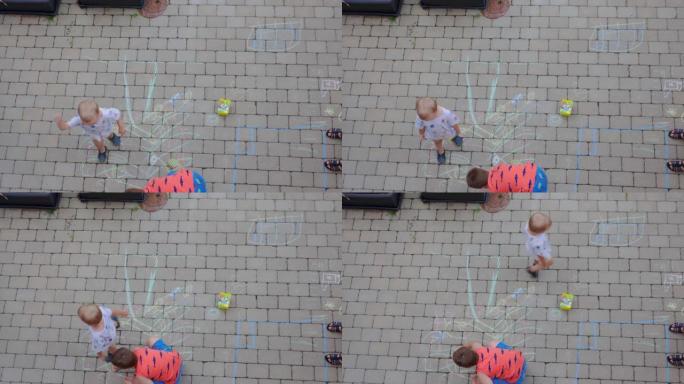 短片显示了两个男孩在用彩色粉笔铺路板上绘画的俯视图。瑞典。
