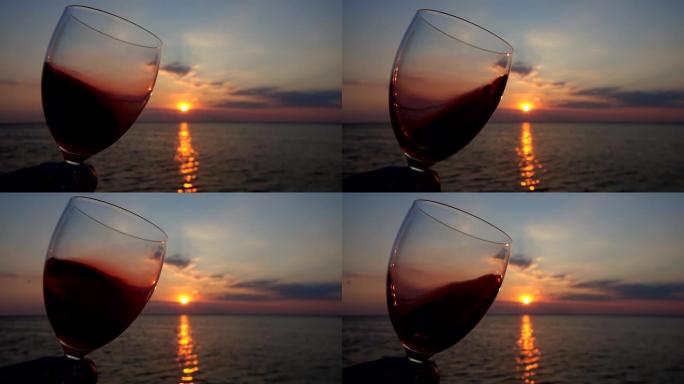 在海上日落的背景下，在玻璃杯中喝酒。慢动作。