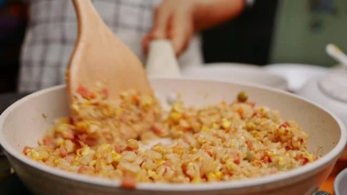 女人在厨房炉子上的煎锅里用蔬菜炒鸡蛋和泰国酱煮自制炒饭。准备健康餐的概念。炒饭的制作过程。