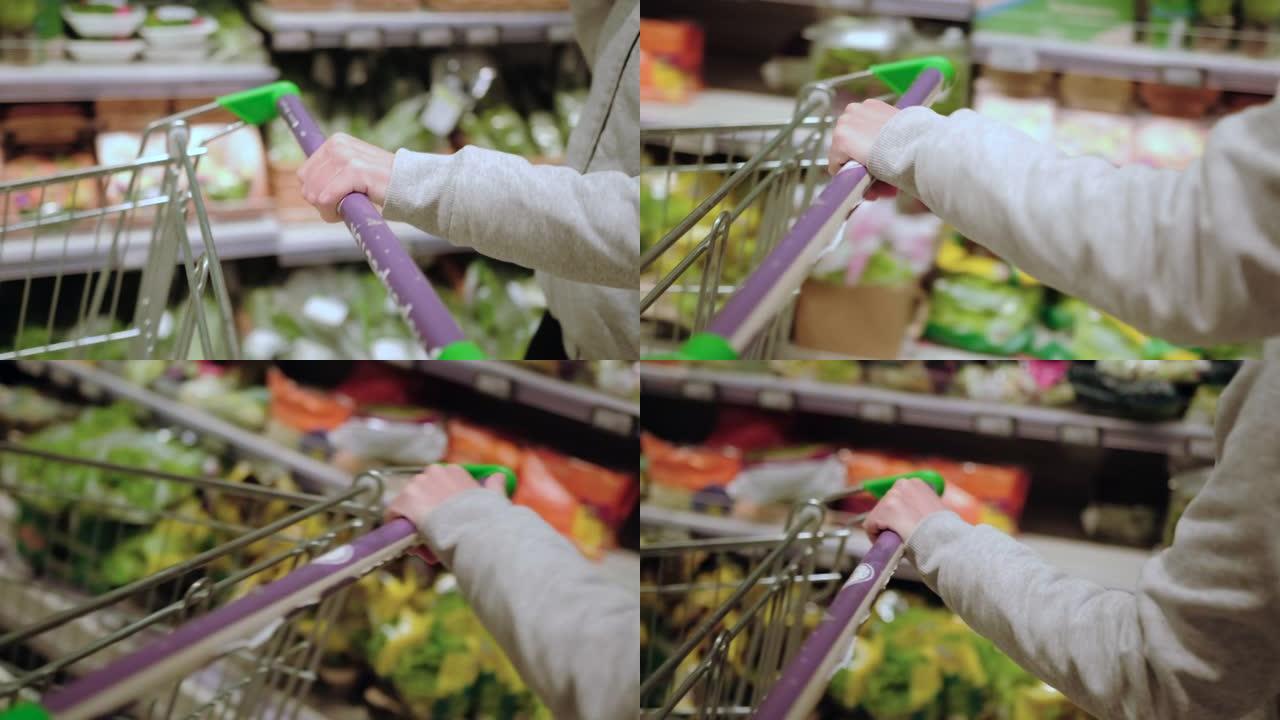 一只手在一家杂货店超市的蔬菜柜台前拿着一辆杂货店车。