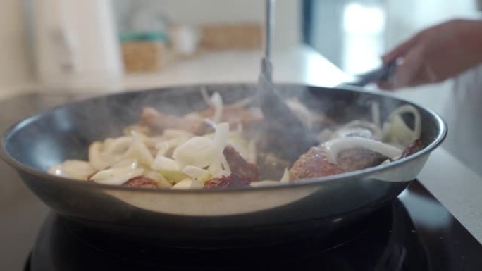 女人在厨房里准备食物，在电炉上的锅里用洋葱炒肉