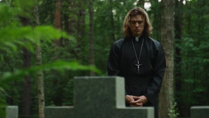 基督教牧师带着十字架在墓地上祈祷。