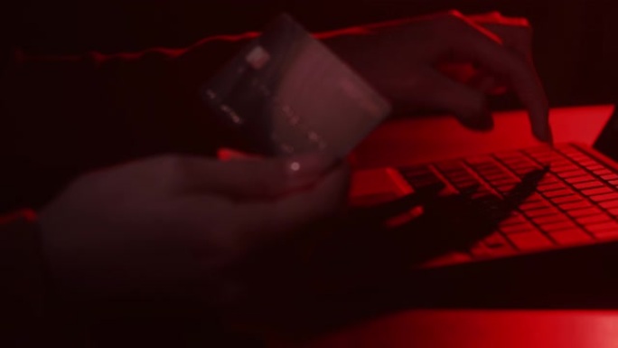 银行诈骗手的信用卡笔记本电脑在暗红色