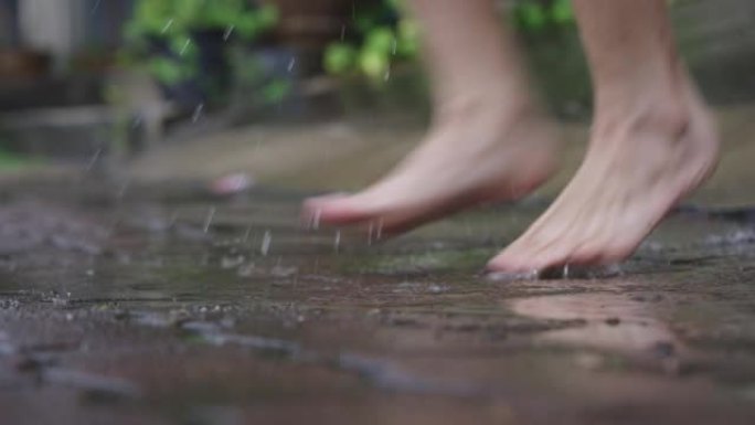 下雨天，女性赤脚在水坑上跳跃和玩耍的低角度，在街道边的人行道上倾盆大雨，有趣的时间泼水，四处跳跃，无