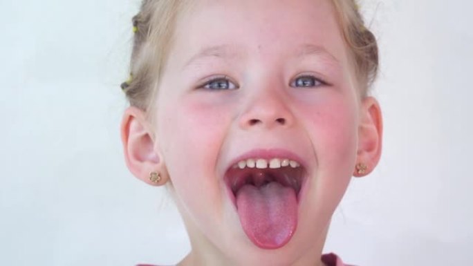 开朗的孩子。女孩在白色背景上笑特写脸。一个小女孩露出舌头喉咙。张大嘴，舌头突出的肖像。清晰的视野拉出
