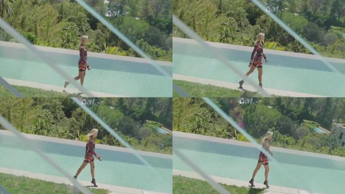 穿着短裙和高跟鞋的迷人女人在游泳池边散步。模型沿着游泳池的边缘与镜子。时尚。一个金发女孩4K