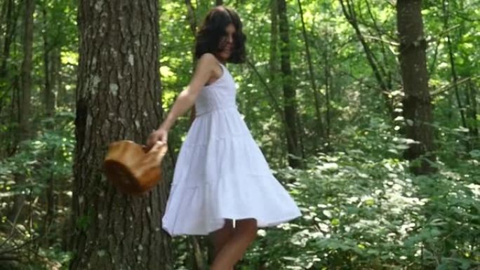 一个快乐的年轻女孩在树林里散步，拿着篮子，惊奇地仰望天空的慢动作镜头