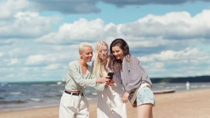 一群快乐的女性朋友在海边为社交媒体拍摄短片。女人用手机摄像头拍摄女友，女孩看镜头和大笑
