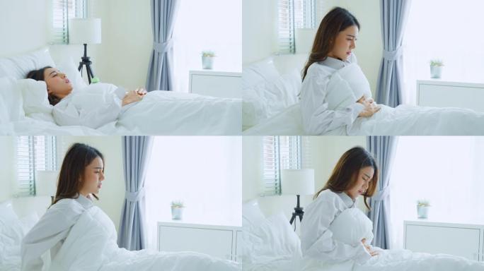 穿着睡衣的亚洲美丽生病的女孩在卧室睡觉。迷人的年轻女子在床上醒来后感到难受和疼痛，胃痛或月经，然后早