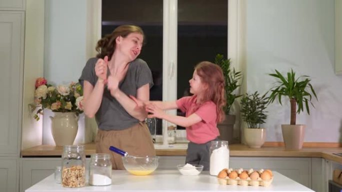 妈妈高五在厨房女儿。一个女人和女孩在白色桌子上煮舞蹈鸡蛋煎蛋卷。天然美食。早餐加牛奶早餐。幸福家庭健