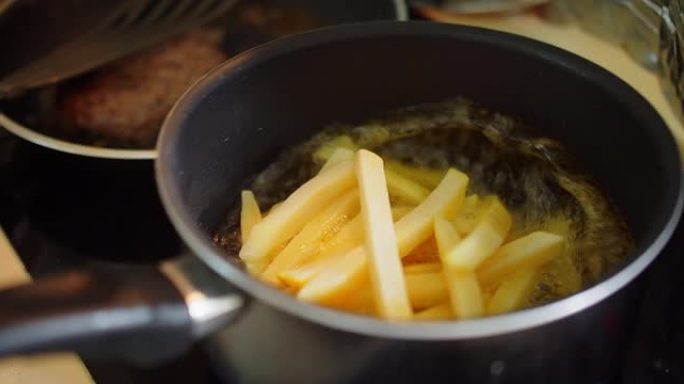 特写烹饪自制油炸黄色炸薯条土豆在厨房热沸腾飞溅油，油炸美味小吃，快餐