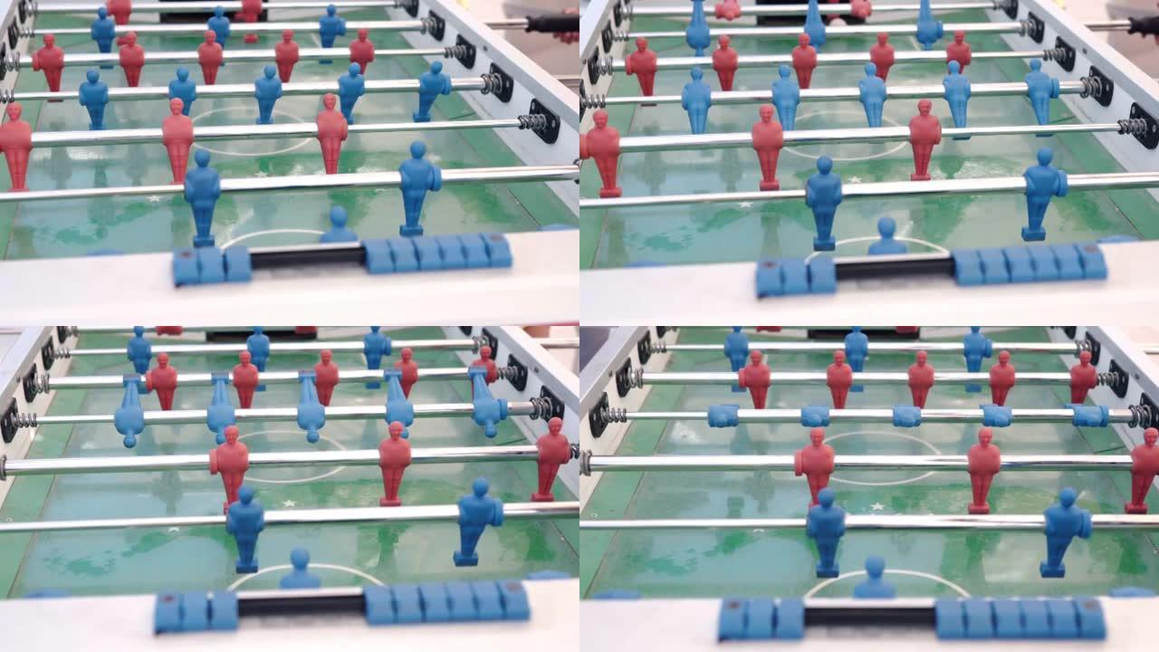 无法识别的人在户外踢桌上足球，带有红色和蓝色塑料雕像的桌板通过人的手踢虚拟足球。微型足球运动员挖白色