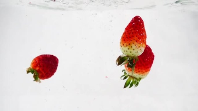 草莓在水中落下并旋转。白色孤立背景上的慢动作。