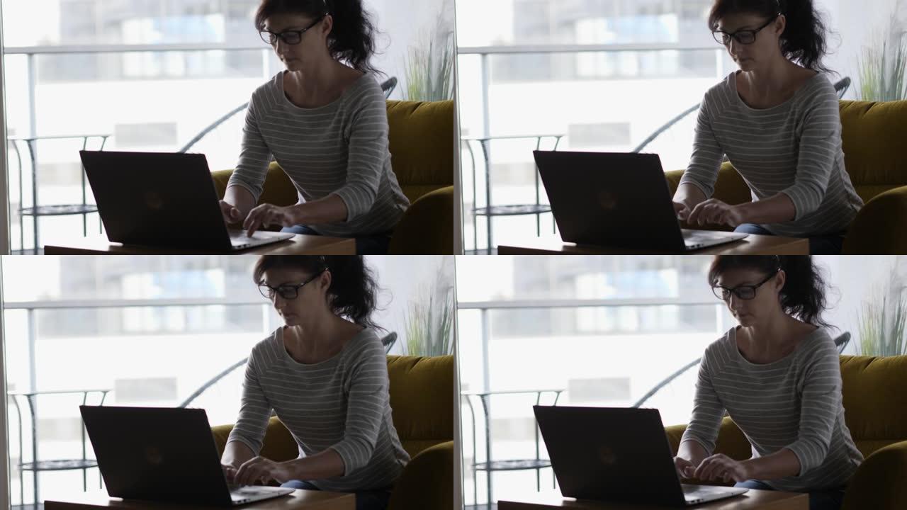 美丽的年轻黑发女商人坐在舒适的椅子上在笔记本电脑上工作。女性在办公室的笔记本上工作，可以看到城市的景