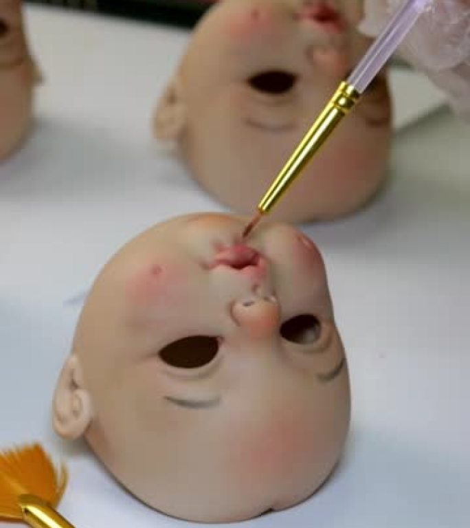 制作洋娃娃。画家大师用细刷子仔细地为洋娃娃涂上空白的嘴唇。工作和爱好相结合的概念。