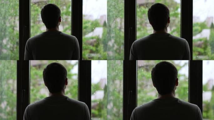 一个男人的剪影看着窗外的雨