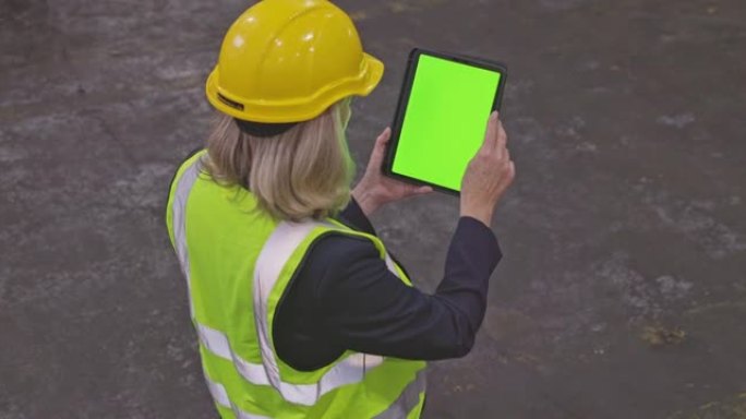 一个成熟女人在仓库中使用带有绿屏的数字平板电脑的4k视频片段