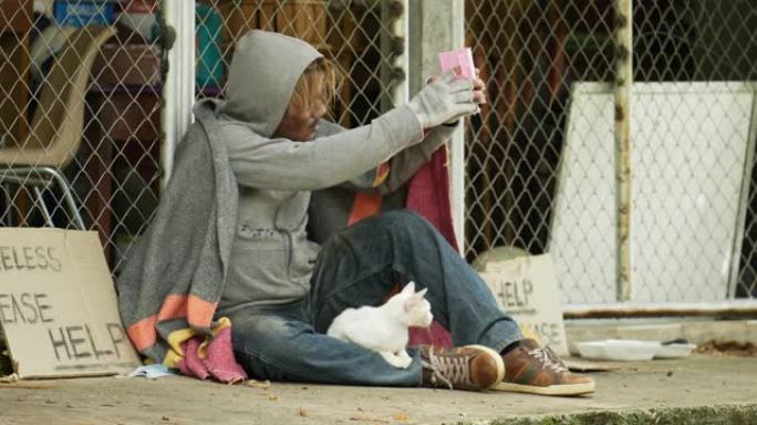无家可归，穿着脏衣服，拿着旧毯子和猫