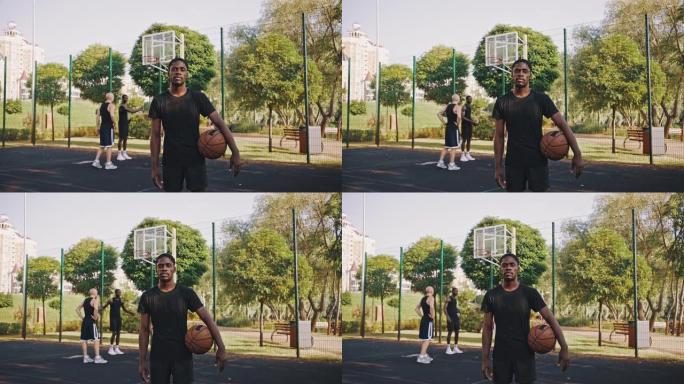 一个带球的黑人篮球运动员的肖像。英俊的非洲裔美国篮球运动员在户外篮球场上站着一个球